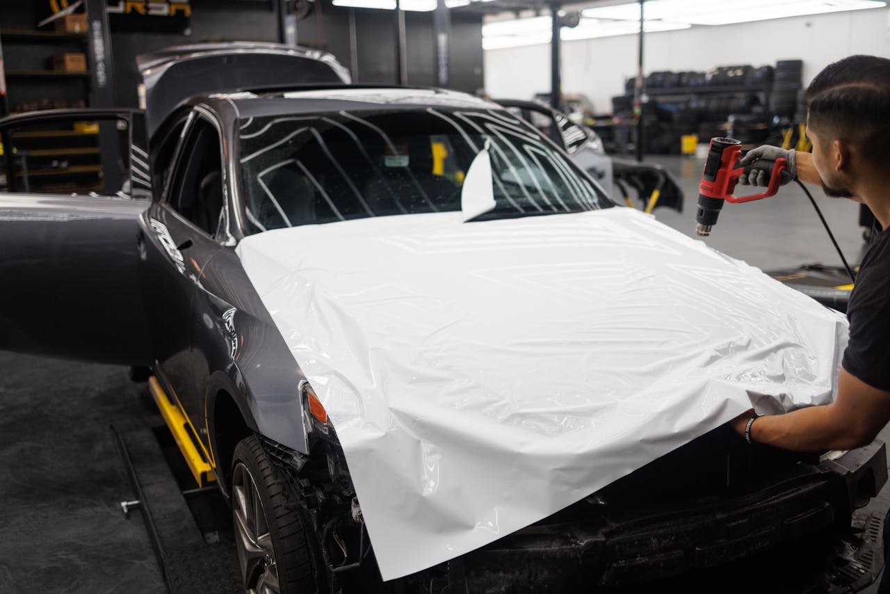 Car being wrapped with white vinyl in an auto workshop by a skilled mechanic.