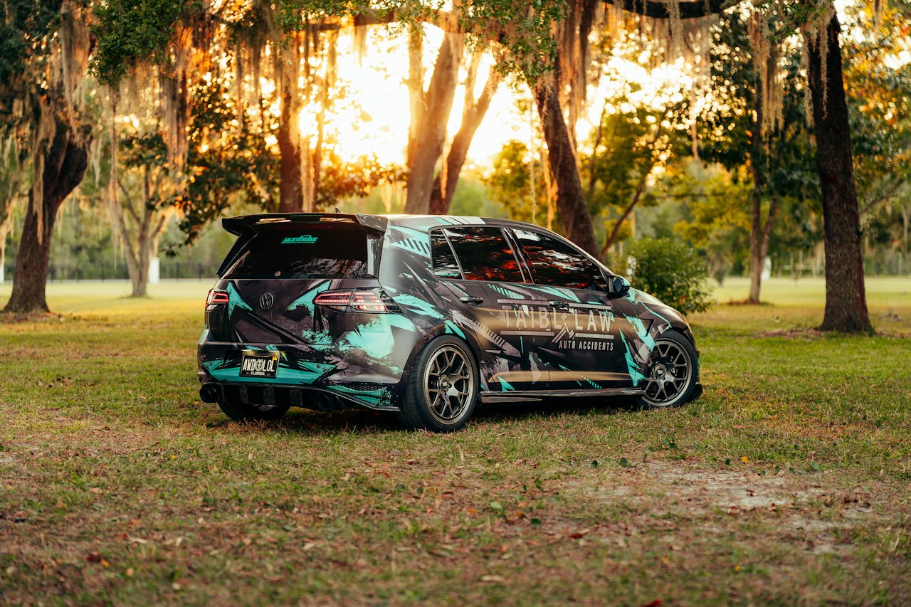 A sporty, custom-wrapped car parked in a tranquil park during a beautiful sunset.